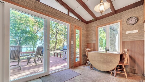 A room with a wooden ceiling, large windows, a wooden table, and a chair.