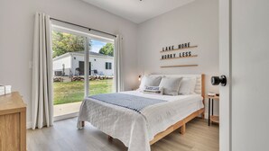 A bedroom with a bed, a bedside table, a nightstand, a sliding glass door to a backyard, and a wall with motivational text. - Cozy 3 bedroom Cabin- Close to splash pad (Spirit Lake)