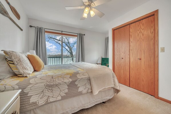 Un dormitorio con cama, ventilador de techo, ventana con cortinas y puerta de madera.