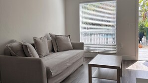 Ett modernt vardagsrum med en soffa, ett soffbord och ett stort fönster med persienner.