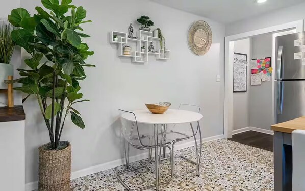 A modern kitchen with a round table, chairs, a refrigerator, and decorative items on the wall.