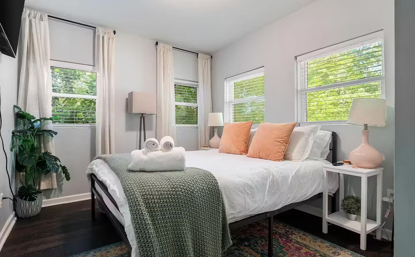 Une chambre à coucher avec un lit, deux tables de chevet, une plante en pot et une fenêtre avec des stores.