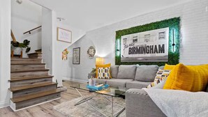 Una sala de estar moderna con una escalera, un sofá, una mesa de centro y una pared con un letrero que dice 'BIRMINGHAM'.