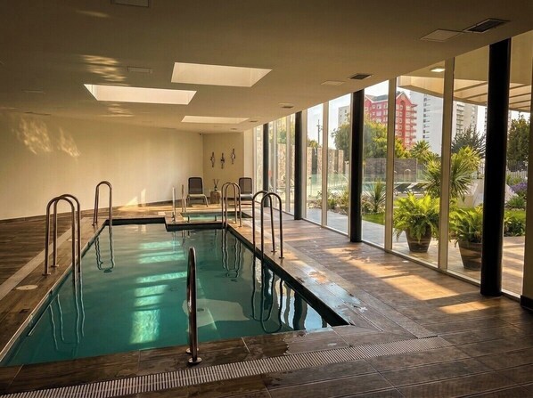 Une piscine intérieure avec des parois en verre transparent, un plancher en bois et une vue sur l’extérieur.