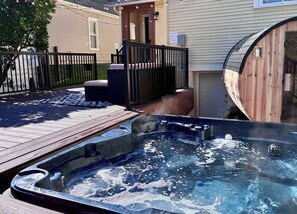 A hot tub in a backyard with a wooden deck, a black fence, and a house in the background.