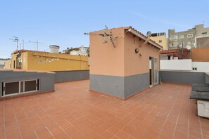 Une terrasse sur le toit avec un sol carrelé, un petit espace clos et un bâtiment doté d’un toit plat et d’une antenne parabolique.
