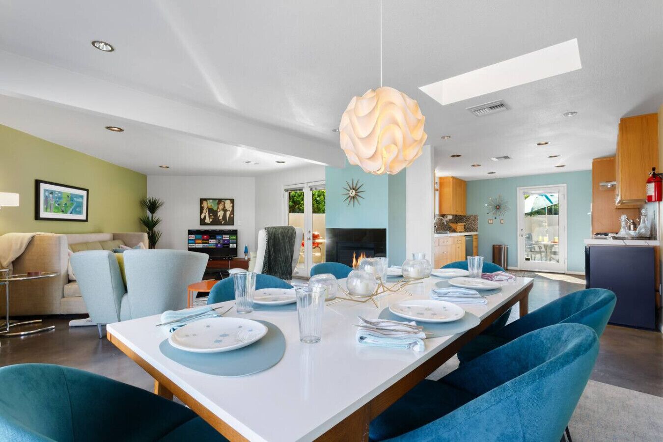 Un comedor moderno con una larga mesa dispuesta para seis personas, sillas tapizadas en azul y una lámpara colgante esférica original.