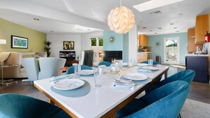 Un espace de salle à manger moderne avec une longue table dressée pour six personnes, des chaises à revêtement bleu et un luminaire suspendu sphérique original.