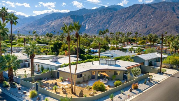 Une maison moderne dotée d’un patio, entourée de palmiers et avec une chaîne de montagnes en toile de fond.