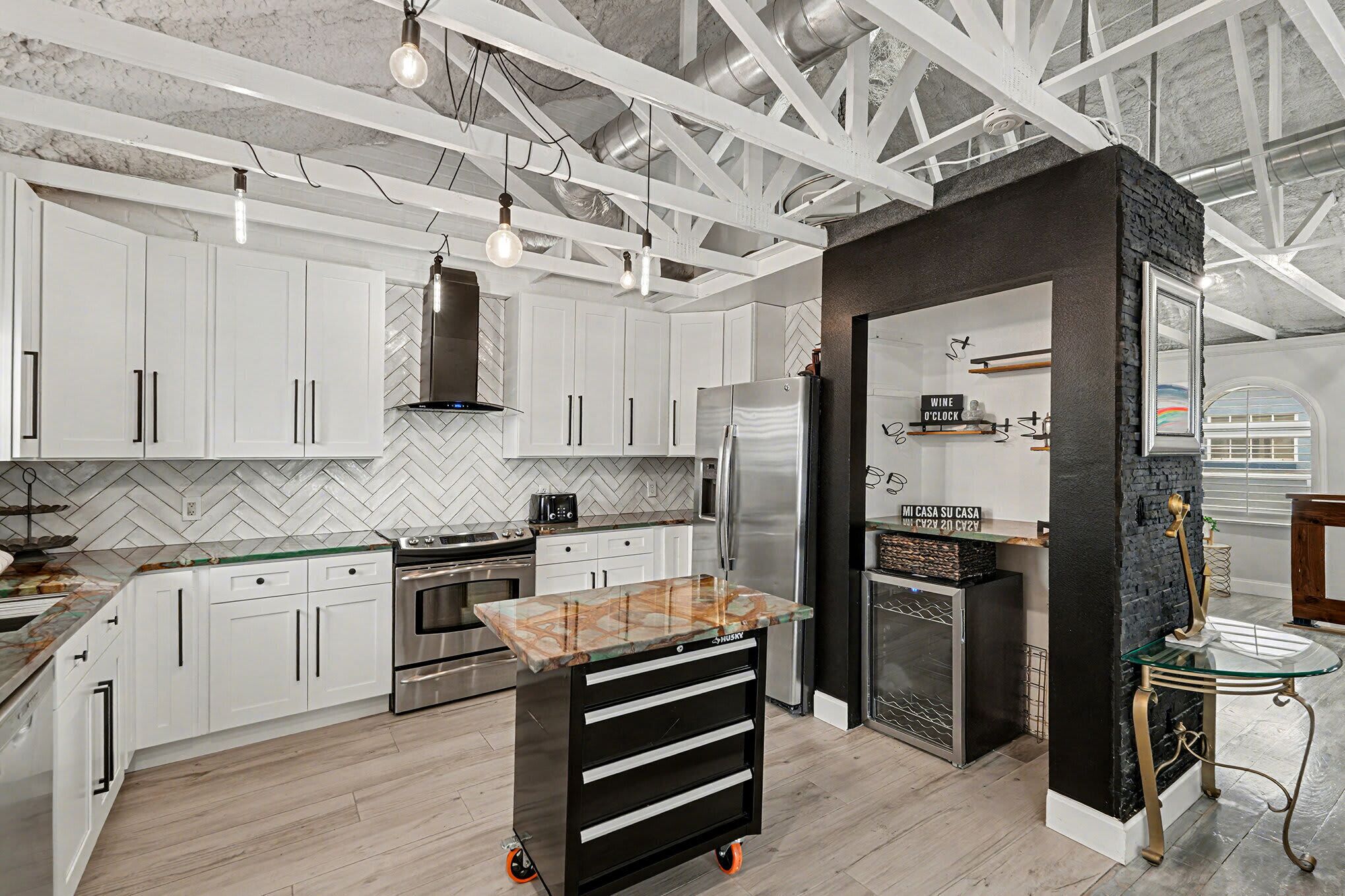 A modern kitchen with white cabinets, a marble countertop island, and a black accent wall.