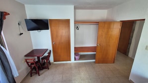 Ein Zimmer mit Holztisch und -stühlen, einem an der Wand befestigten Fernseher und einem Kleiderschrank mit Sitzbank darin.