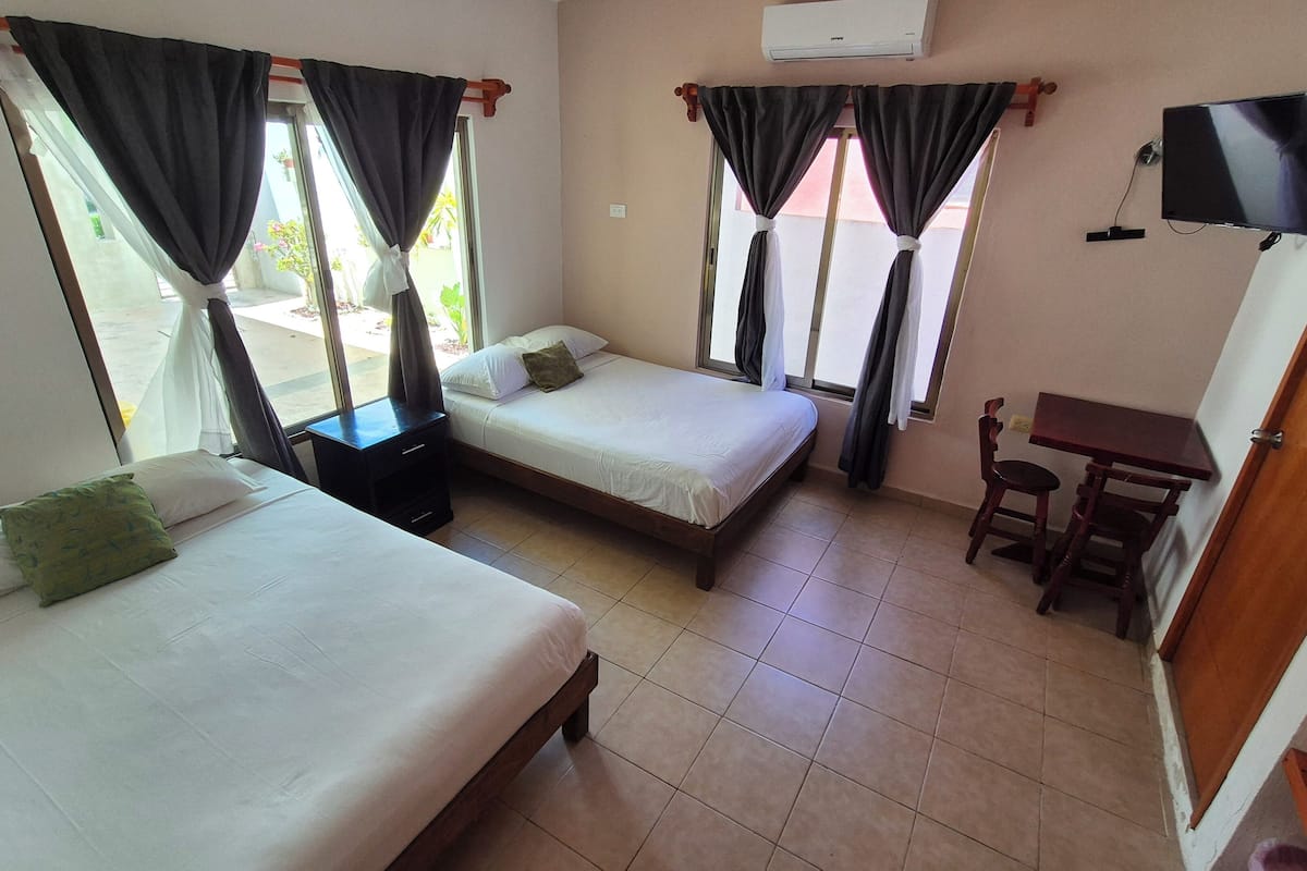 A hotel room with two beds, a TV, a small table, and curtains.