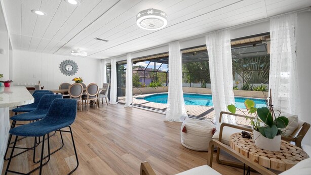 Ett rymligt inomhusområde med en pool, trägolv och en matplats med blå stolar och ett vitt bord.