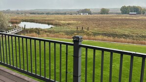 A deck with a view of a grassy field, a small body of water, and distant trees. - Ranch house in Arimo, Idaho with beautiful views, huge yard, and room to gather. (Arimo)