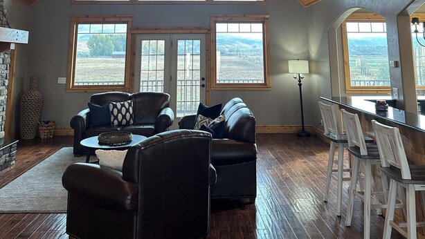 A spacious living room with a high wooden ceiling, large windows, and a view of the outdoors. - Ranch house in Arimo, Idaho with beautiful views, huge yard, and room to gather. (Arimo)