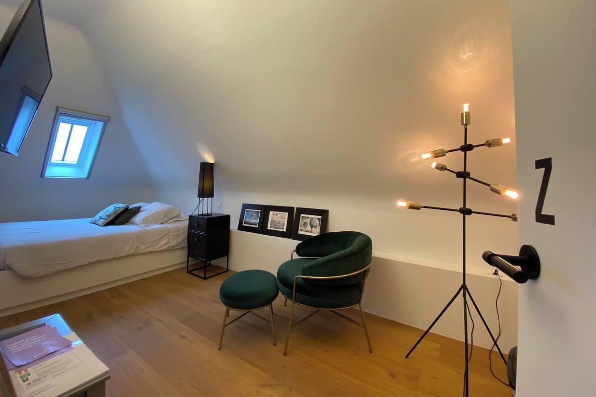 A bedroom with a bed, a desk, a chair, a lamp, and a wall-mounted light fixture.
