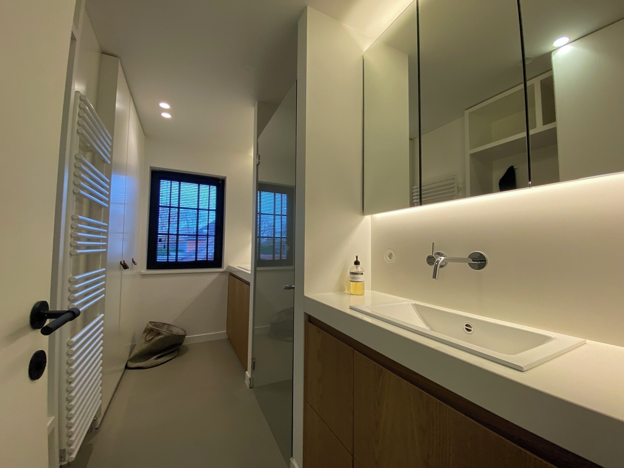 A modern bathroom with a large mirror, a white sink, and a window with blinds.