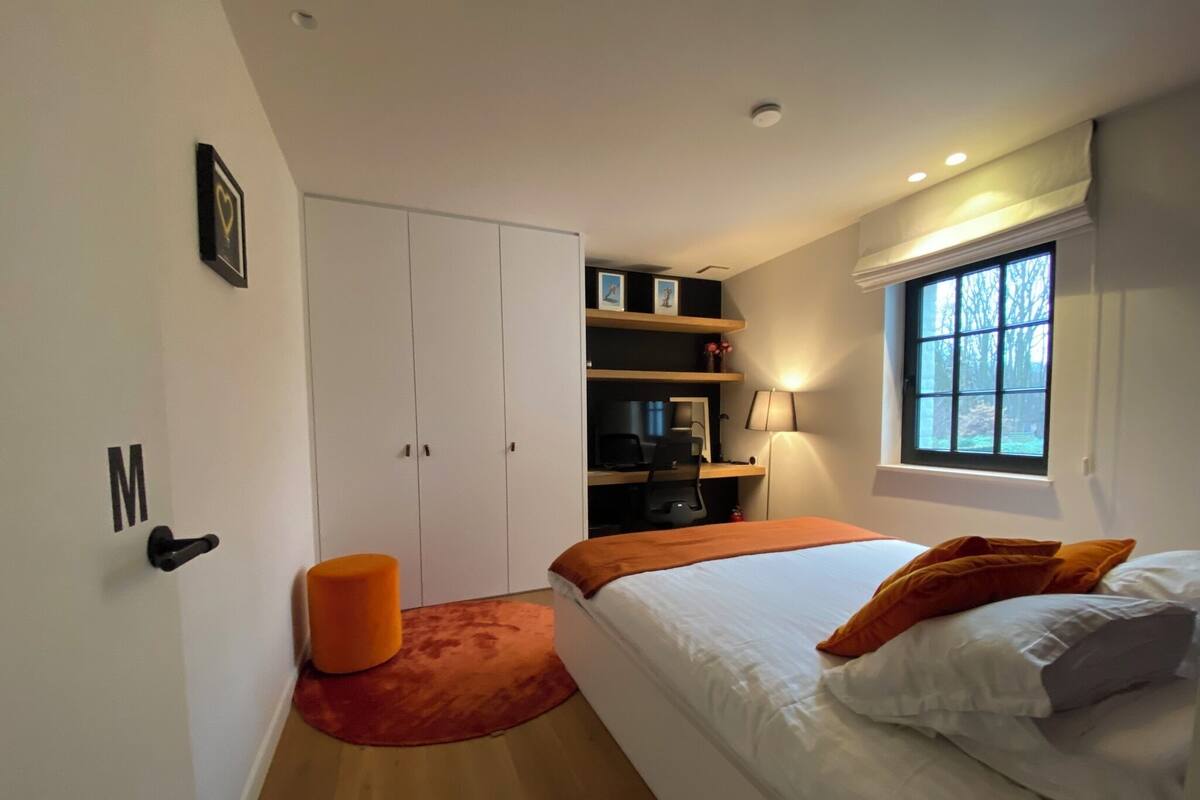 A bedroom with a bed, a desk, a wardrobe, and a window.