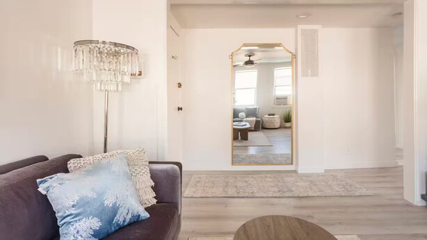 Una sala moderna con un sofá marrón oscuro, una almohada decorativa azul, una lámpara de pie y un espejo grande que refleja un comedor.