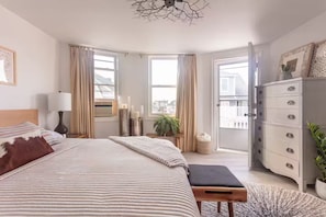 Ein Schlafzimmer mit einem großen Bett, Nachttischen, einem Schminktisch und Blick auf die Stadt durch große Fenster.