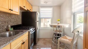 Una cocina compacta con armarios de madera, un refrigerador negro, una estufa y un pequeño comedor con una mesa redonda y dos sillas.