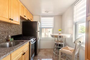 A compact kitchen with wooden cabinets, a black refrigerator, a stove, and a small dining area with a round table and two chairs. - Luxurious Beachside retreat, 2 Bedrooms Entire rental unit in Queens, New York (Rockaway beach)