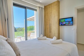 Quarto de hotel com uma cama grande, uma televisão fixada na parede e vista para o exterior.