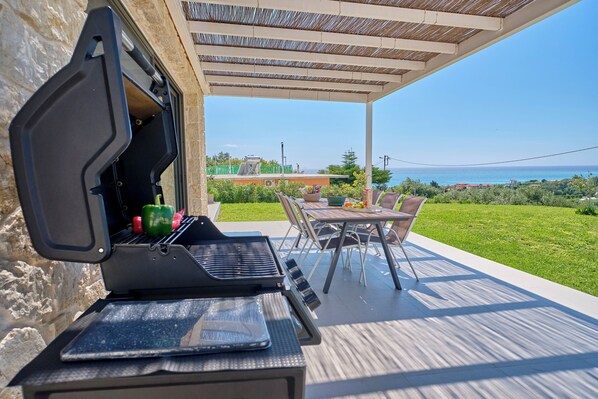An outdoor patio with a grill, a table, and chairs, overlooking a scenic view.