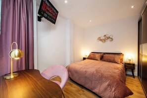 Une chambre à coucher comprenant un lit, des tables de chevet, un bureau, une chaise et un téléviseur fixé au mur.