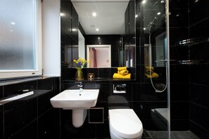 Une salle de bain moderne avec un lavabo blanc, des toilettes et une douche séparée par une paroi de verre.
