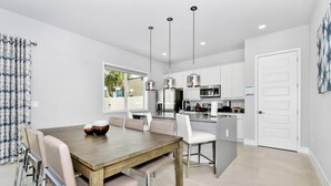 Eine moderne Küche mit Edelstahlgeräten, ein Essbereich mit Holztisch und Stühlen sowie ein Ausblick ins Freie durch ein großes Fenster.