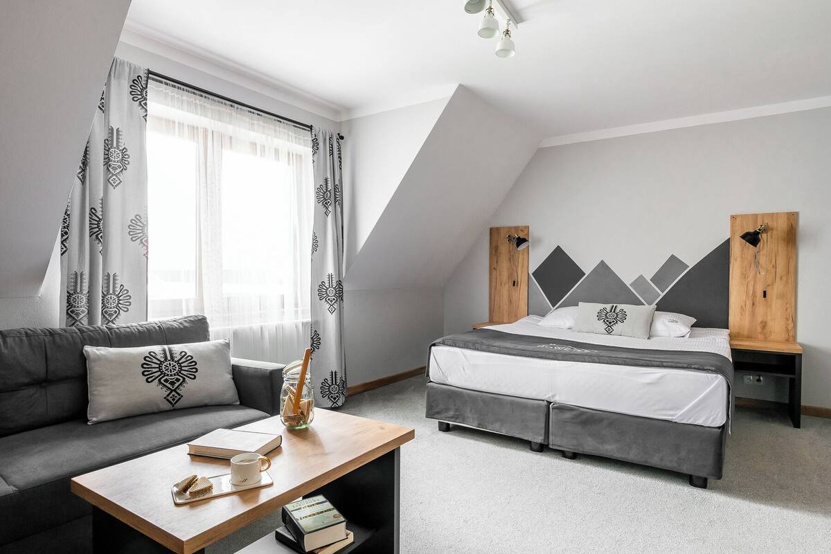 Ein modernes Schlafzimmer mit Bett, einer Couch, einem Couchtisch und einem Fenster mit Vorhängen.