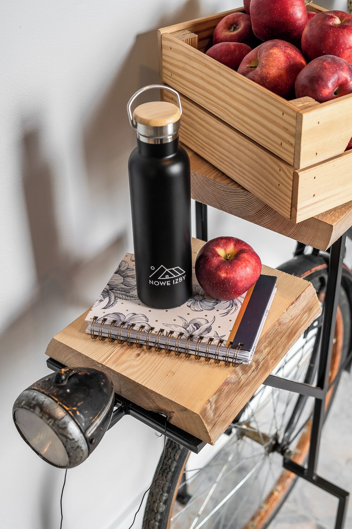 A bicycle with a wooden crate of apples, a black water bottle, and a notebook on the seat.