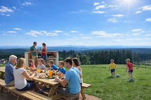 A group of people dining outdoors with a scenic view of mountains and a clear sky.