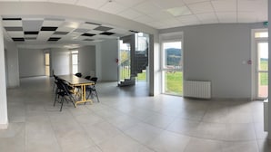 A spacious room with a conference table and chairs, large windows with a view of the countryside, and a staircase leading to an upper level. - Group and stopover gîte in the heart of nature, on the Chemin de St Jacques GR65-GR7 (Riotord)