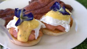 Un plato con dos sándwiches huevos benedictinos y una guarnición de tocino.