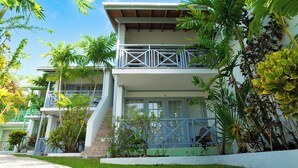 A two-story building with a balcony on the upper floor, surrounded by lush greenery. - Sunset Lane (Holetown)