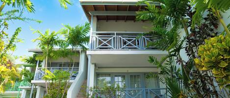 A two-story building with a balcony on the upper floor, surrounded by lush greenery.