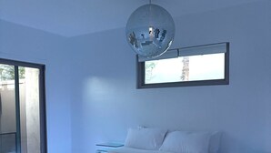 A modern bedroom with a large bed, a ceiling disco ball, a window, and a glass table beside the bed. - Retro Retreat w/ Hot Tub + Sunset Views (Borrego Springs)