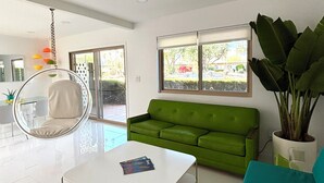 Een moderne woonkamer met een hangstoel, een groene bank, een witte salontafel en een grote potplant.