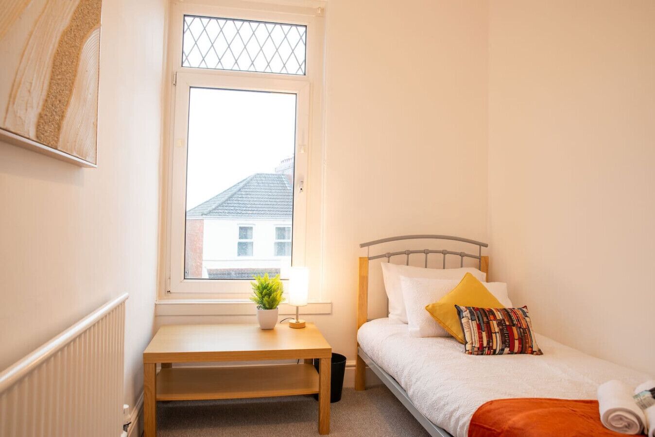 Een slaapkamer met een bed, nachtkastje met lamp, raam en een radiator.