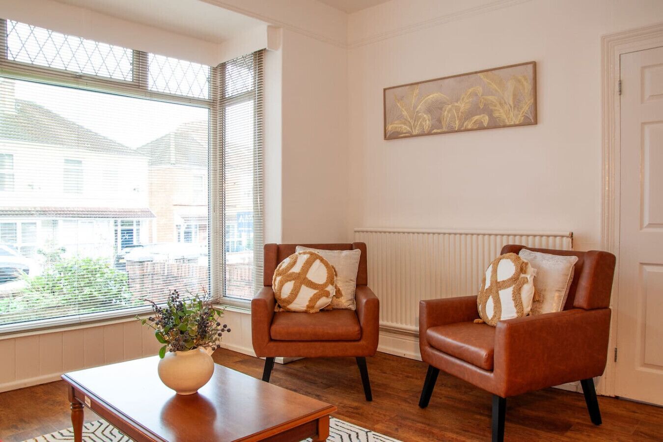 A room with two leather armchairs, a wooden coffee table, a vase with a plant, and a painting on the wall.