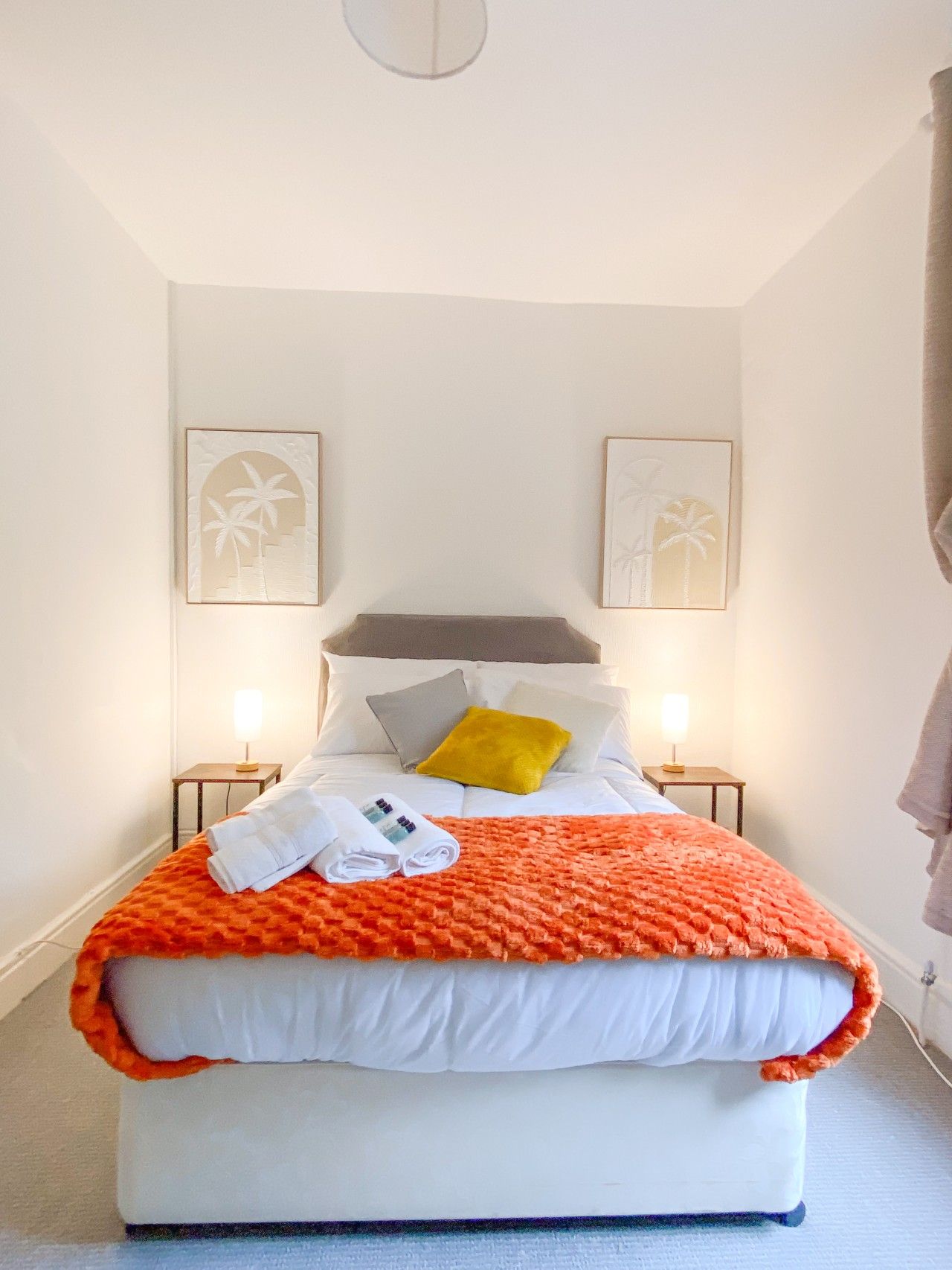 A neatly made bed with a white and orange blanket, two pillows, and a folded towel on a white mattress.