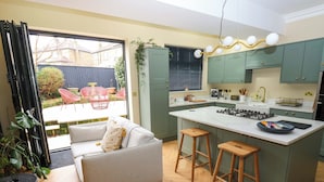 Eine moderne Küche mit einer Kochinsel, Holzbarhocker und einem Sofa mit gelben Kissen.