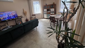 Una sala de estar con un sofá, una mesa de comedor con sillas, un televisor y una planta en maceta.