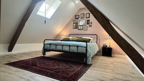 Un dormitorio con techo inclinado, una cama con colcha estampada, una alfombra roja y marcos de cuadros sujetos a la pared.