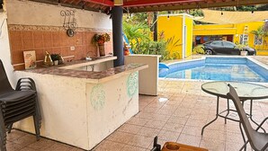 An outdoor bar area with a pool, a wooden table, and a grill. - La Casa Amelia (Nueva Gorgona)