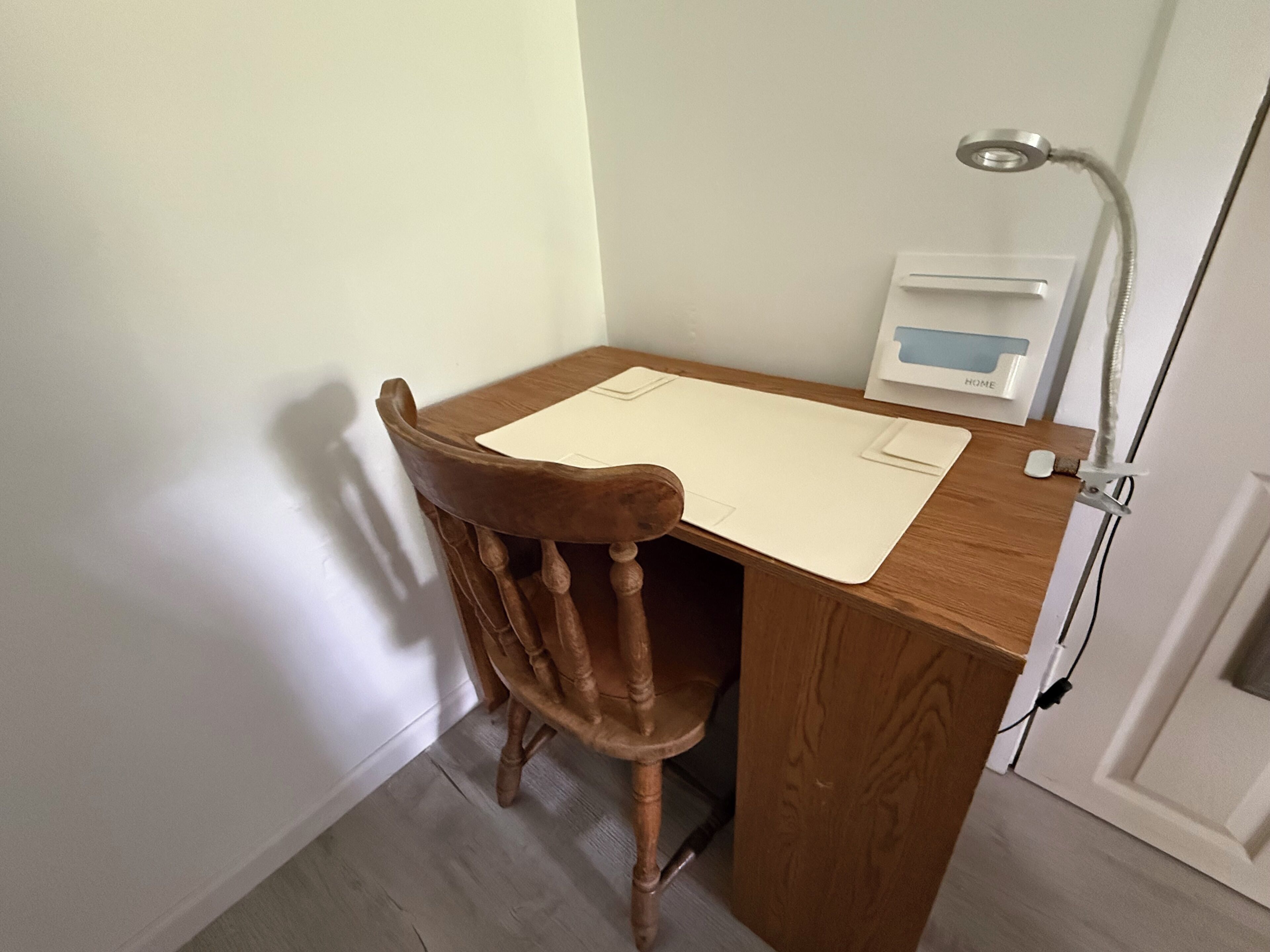 A wooden desk with a chair, a desk lamp, and a small white box labeled "HOME" on the wall.
