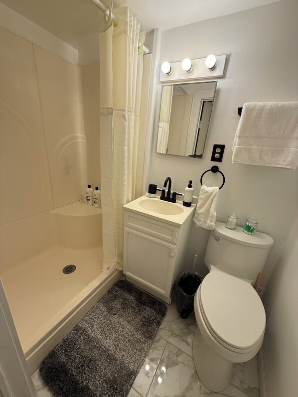 A bathroom with a bathtub, sink, toilet, and a mirror with lights above.