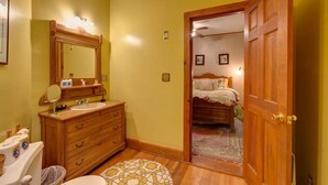 Un dormitorio con puerta de madera, cama con cubrecama floral y baño con tocador de madera y espejo grande.